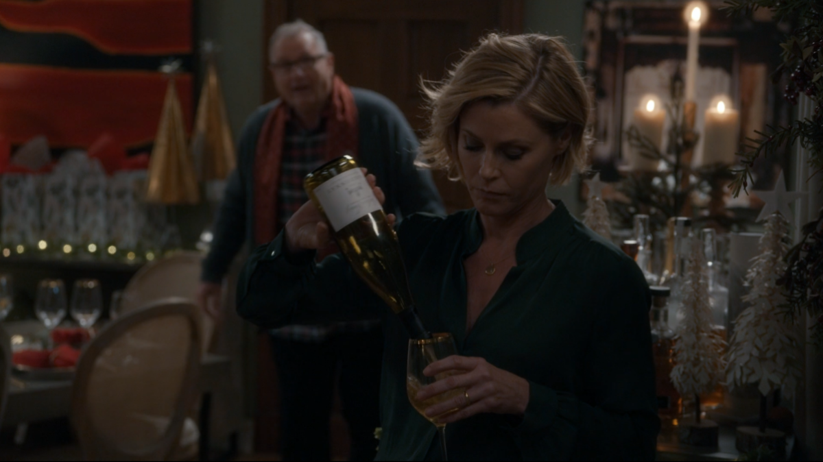 Claire Dunphy pouring a bottle of wine into her wine glass. She's looking down at the glass.